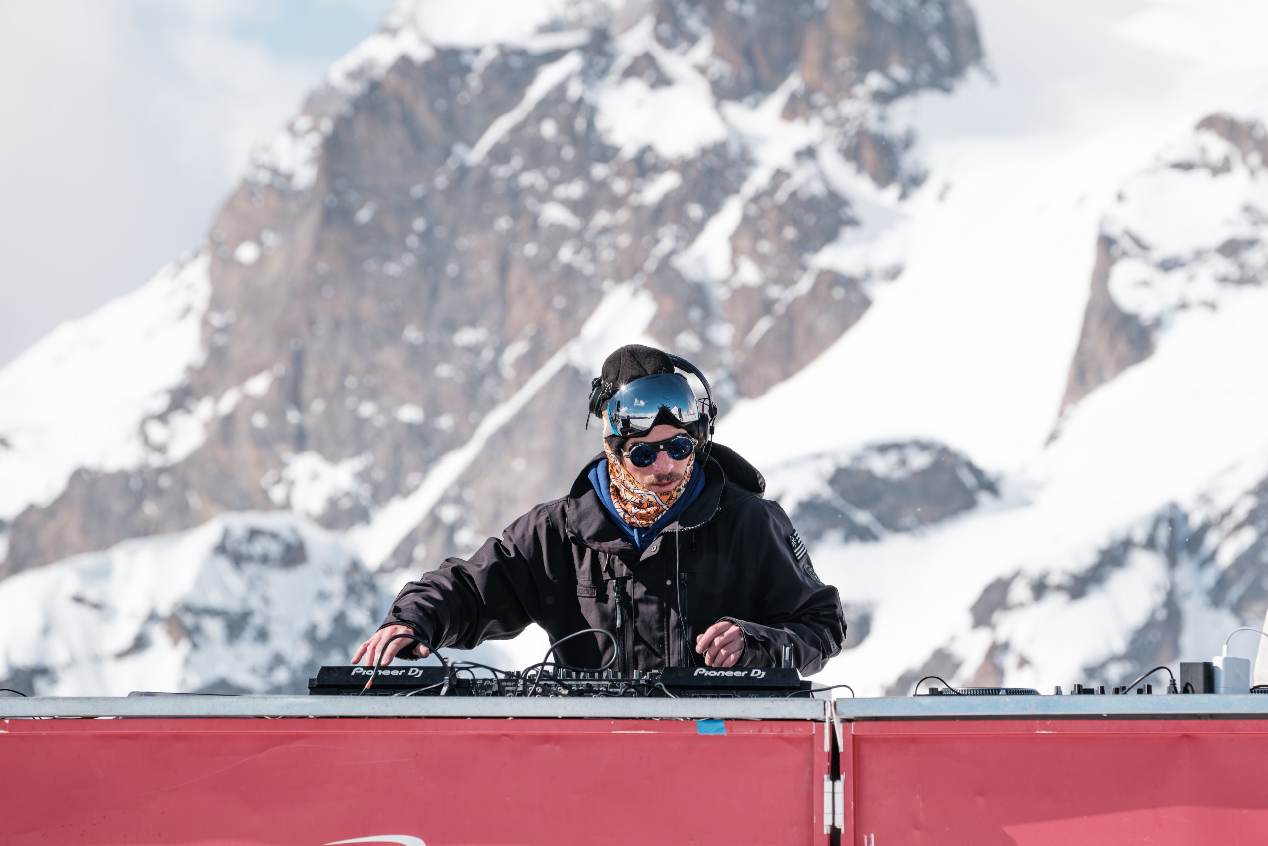 DJ aux platines en altitude, devant une montagne enneigée