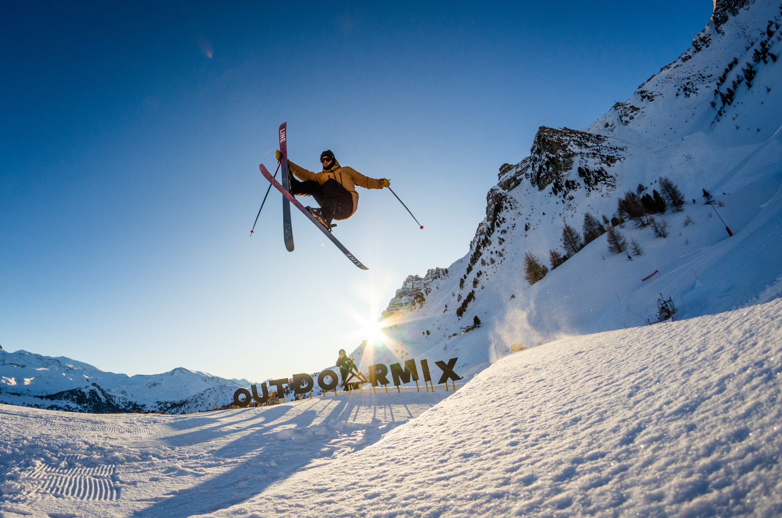 Skieur en plein saut, skis croisés, au-dessus des lettres Outdoormix dans la neige
